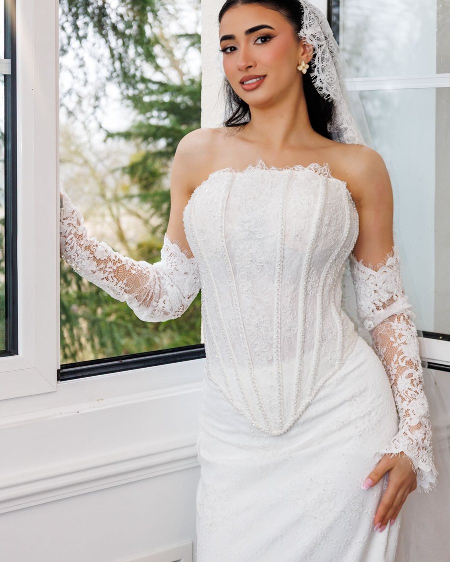 Robe de mariée en dentelle portée près d'une fenêtre, manches longues