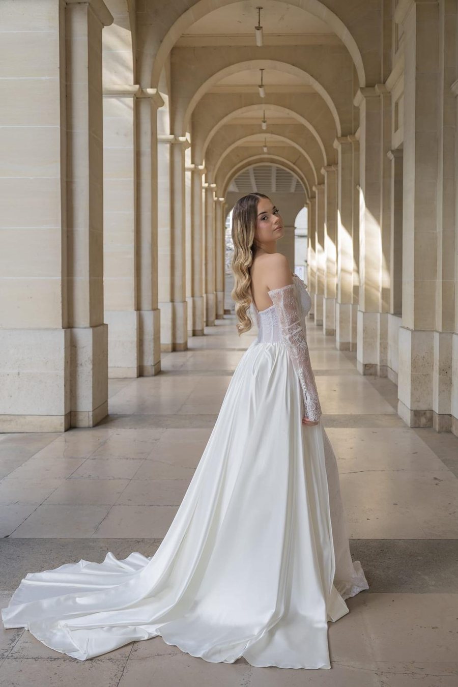 Mariée de dos en robe de satin à traîne, sous une galerie à arcades