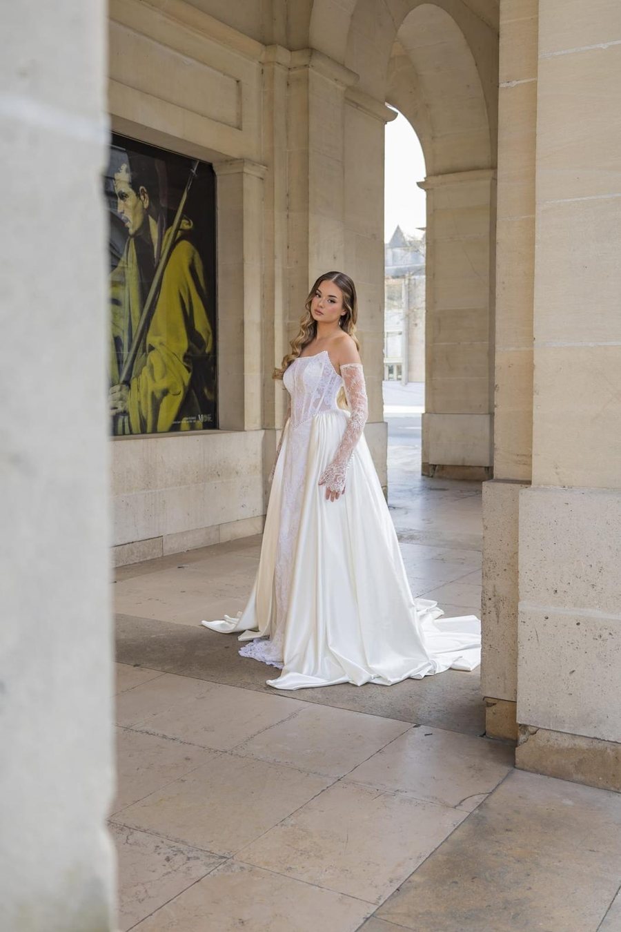 Mariée en robe bustier de dentelle, sous une arcade de pierre claire