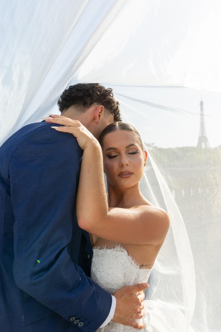 Mariés enlacés sous un voile en tulle, tour Eiffel en arrière-plan