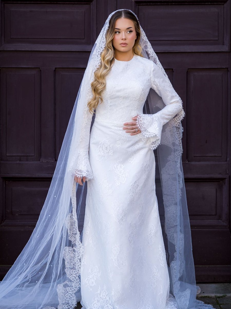 Mariée en robe de dentelle et voile long, devant une porte ancienne