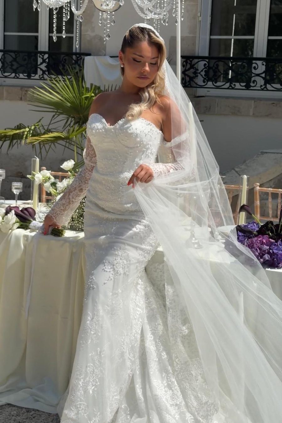 Mariée ajustant son voile, robe sirène en dentelle, table dressée en arrière-plan